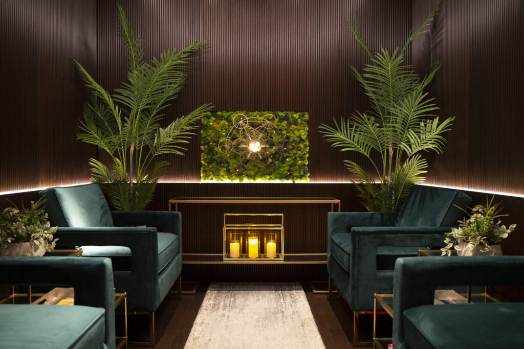 waiting room with four luxurious green velvet chairs with wooden panelling on wall and surrounding plants and candles