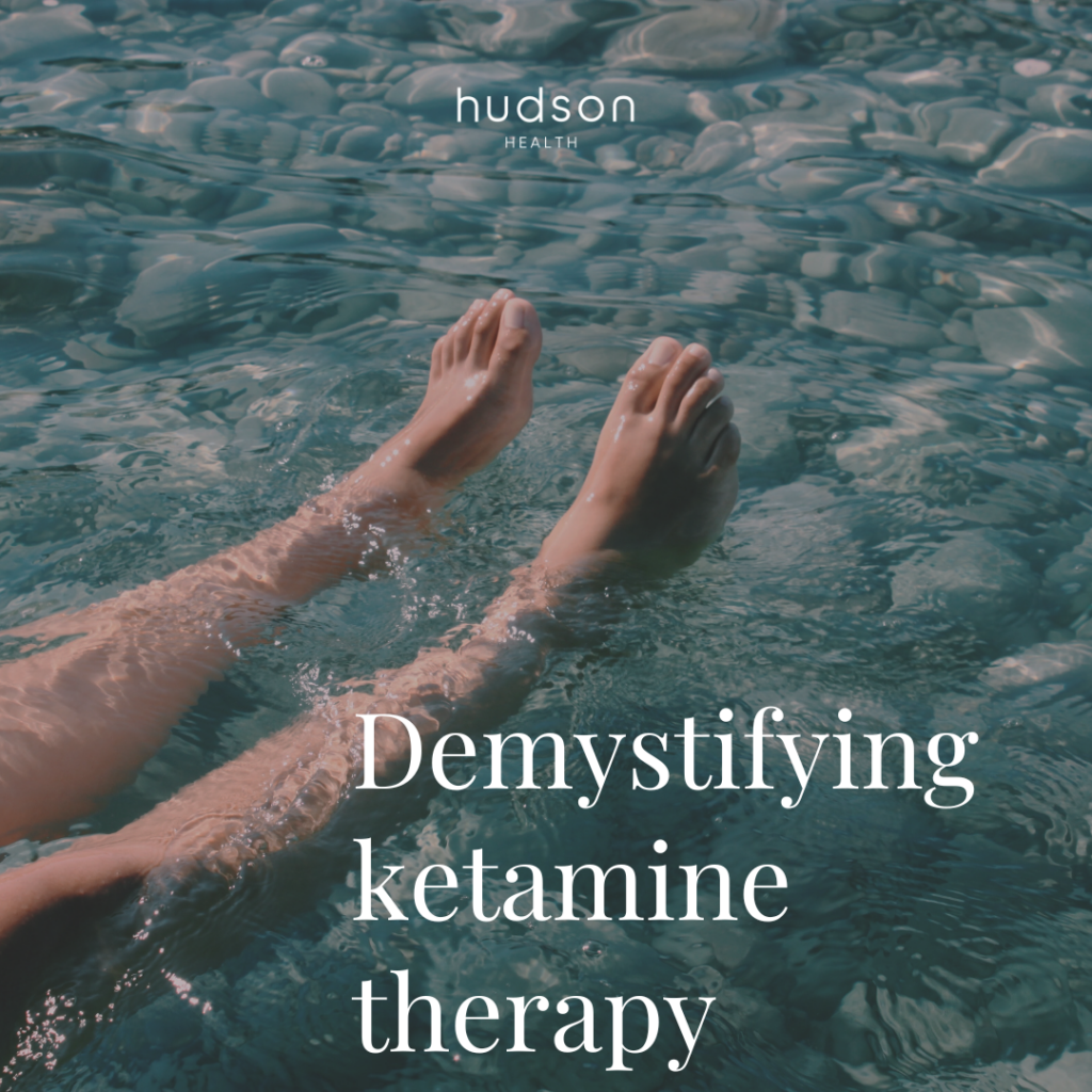 close-up of a person's floating legs in clear water above a rock bottom. The title, Demystifying Ketamine Therapy, is overlaid across the bottom of the image.