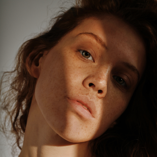 light skin woman with slightly curly hair, no makeup, and freckles looking into camera with a slit of light highlighting right eye