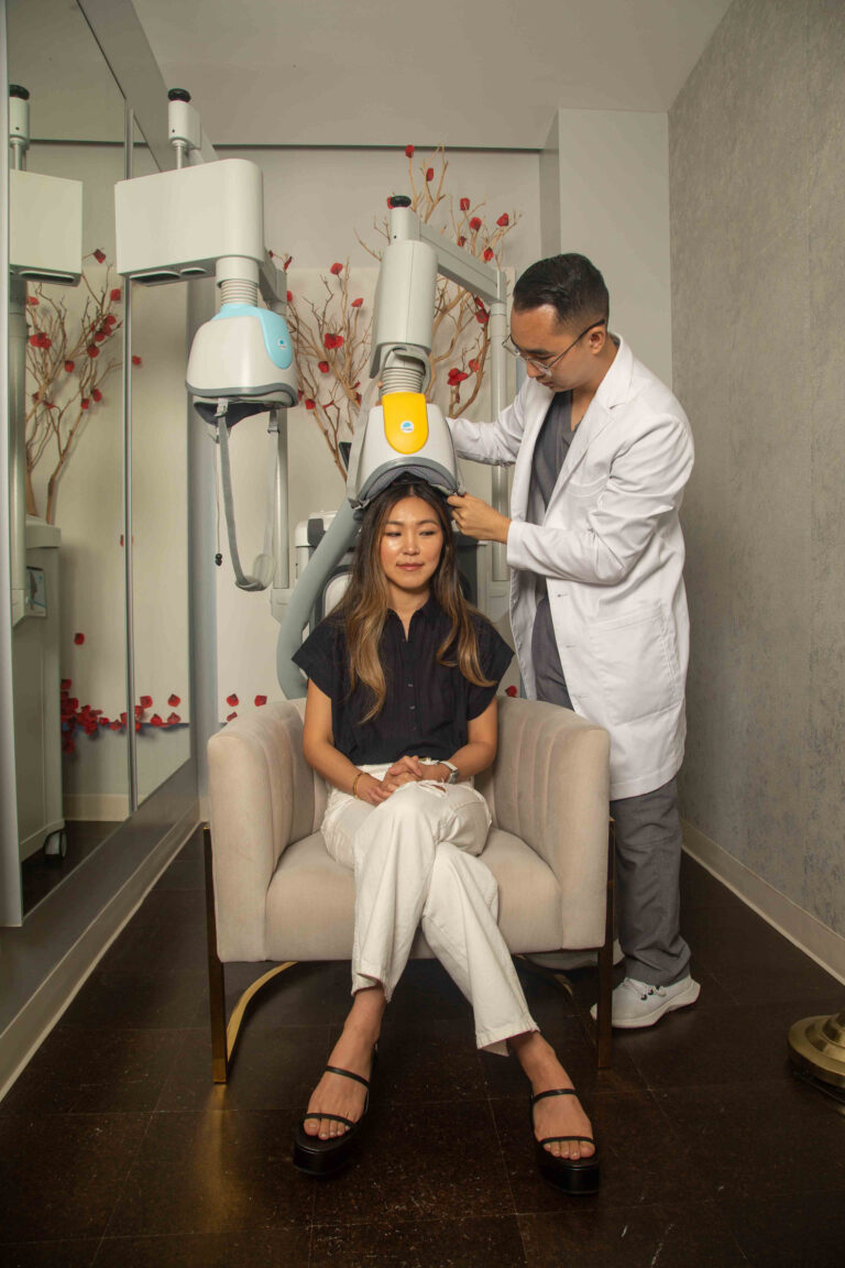 A woman sits in a char while a male Physician Assistant places a Transcranial Magnetic Stimulation (TMS) helmet on her head