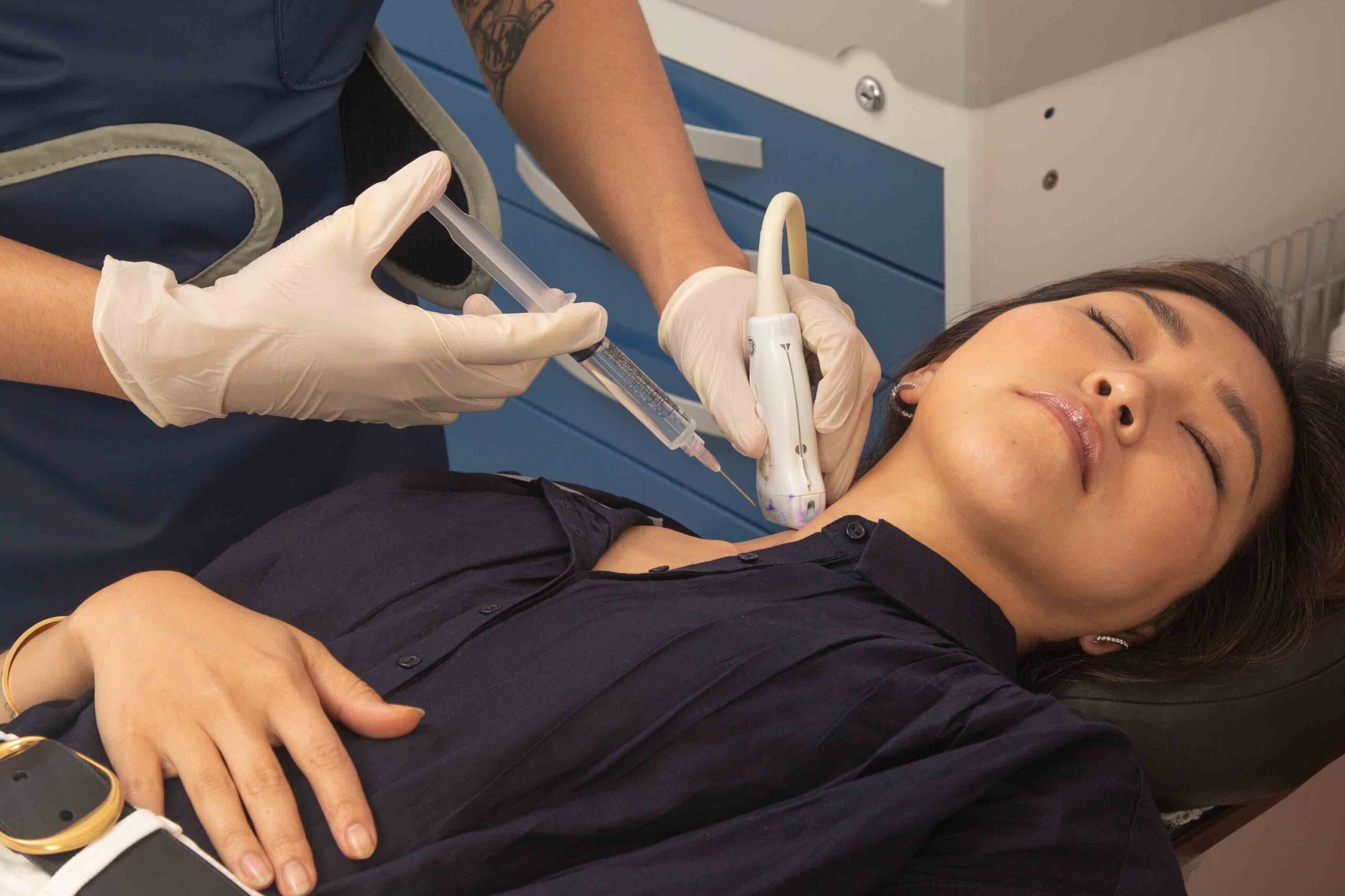 A woman lies on a table as a Doctor administers a Stellate Ganglion Block injection on the side of her neck with the help of Ultrasounds technology to guide the injection.